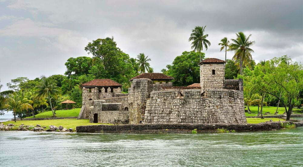 One of the most beautiful places in Guatemala--the Castle of San Felipe de Lara--is shown surrounded by the pretty waters of Lake Izabal and lush greenery