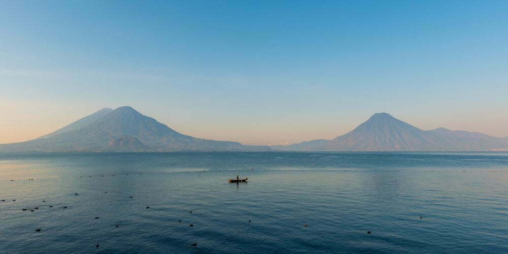 Beautiful Lake Atitlan Guatemala on a misty morning with volcanoes in the background tinted pink from the sunrise. This is one of the most beautiful places in Guatemala
