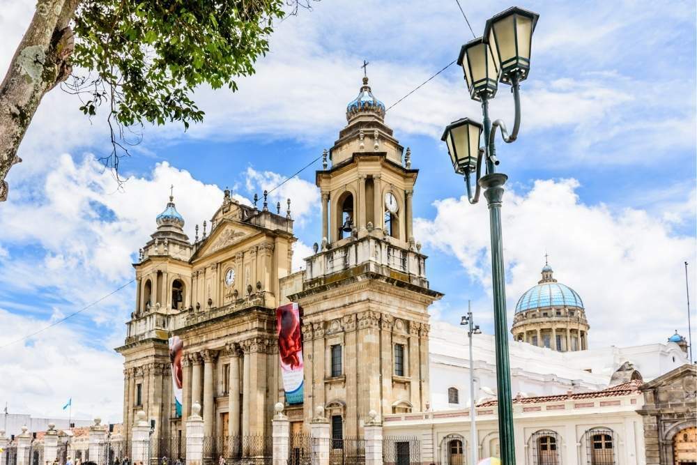 An image of a creme Neoclassical building Metropolitan Cathedral of Guatemala City in Parque Central or Plaza de la Constitución surrounded by a blue sky is one of the most beautiful places in Guatemala to visit