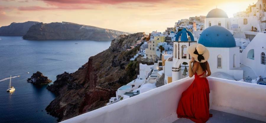 Sexy Outfits for Greece with a woman wearing a red dress in Santorini Greece overlooking the cliffs and ocean
